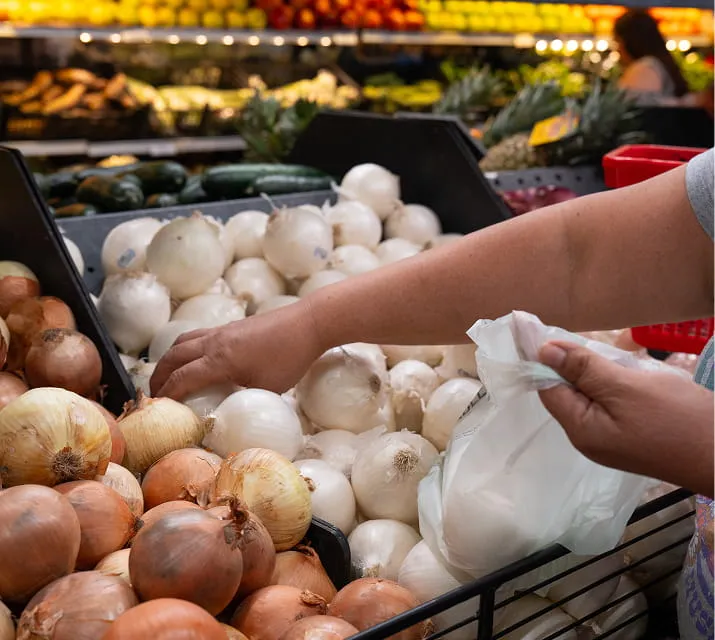 Customer selecting fresh onions in the produce section at Juniors Market