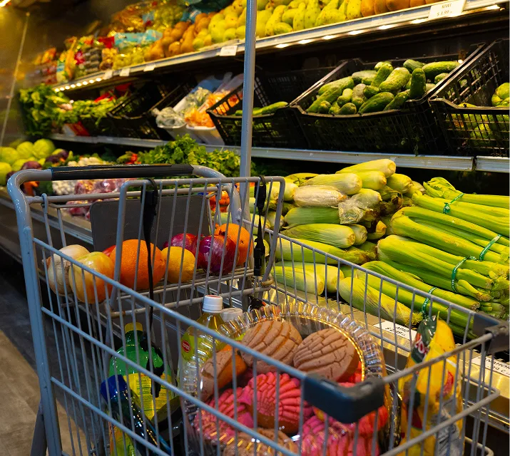Shopping cart filled with fresh fruits and groceries in the produce section at Juniors Market